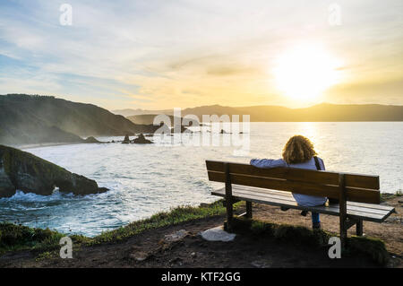 Solo Frau an einer Bank bei Sonnenuntergang am Loiba Felsen (Acantilados de Loiba) Provinz A Coruña, Galicien, Spanien, Europa Stockfoto