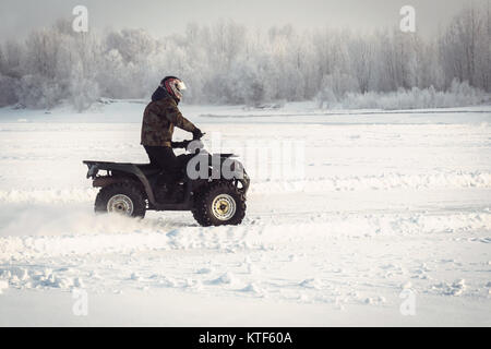 Winterspaß auf dem ATV. Ein Fischer reitet auf dem zugefrorenen See im Winter quartro Bike auf dem Hintergrund der schönen Winterlandschaft mit Schnee t Stockfoto