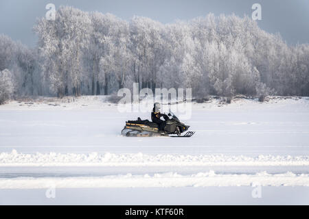 Motorschlitten auf dem Schnee. Treiber von einem Schneemobil in Richtung Süden auf dem zugefrorenen See auf dem Hintergrund der Winter Forest. Treiber in einem schwarzen Outfit auf einem Stockfoto