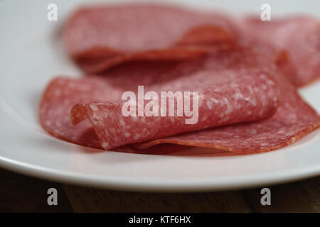 Salami in Scheiben geschnitten auf weiße Platte auf Holz Tisch Stockfoto