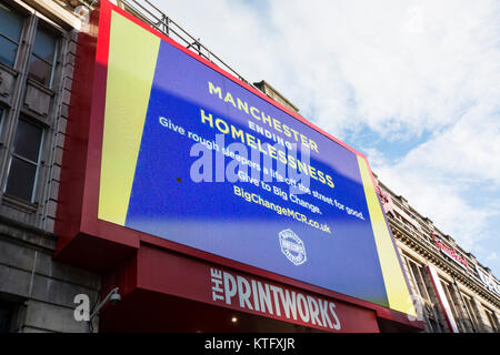 Manchester UK; 25. Dezember 2017: Manchester Rough Sleepers in Manchester am Weihnachtstag. Beleuchtetes Schild auf der Printworks, ehemals Sitz der Manchester Guardian, Werbung, dass Manchester City Plan des Rates, die mit Obdachlosen in Manchester zu beschäftigen. Kerben der Obdachlosen Rough Sleepers verbringen ihr Weihnachten kauerte im shop Türen. Mehrere Passanten angehalten, mit Ihnen zu sprechen, einige mit Kaffee und Essen von den nahe gelegenen Filialen von Starbucks, während eine Mutter und Tochter ihre van im Piccadilly geparkt, die Kleidung zu den Obdachlosen von hinten ihre van Hand. Stockfoto