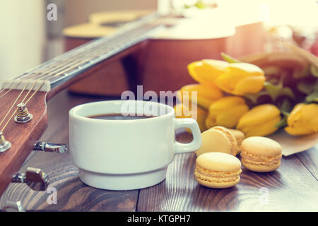 Schöner Frühling Musik Hintergrund. Tasse coffww, Gitarre, gelbe Tulpen, musikalische Seite auf einem dunklen Hintergrund. Geringe Tiefenschärfe. Färbung ph Stockfoto