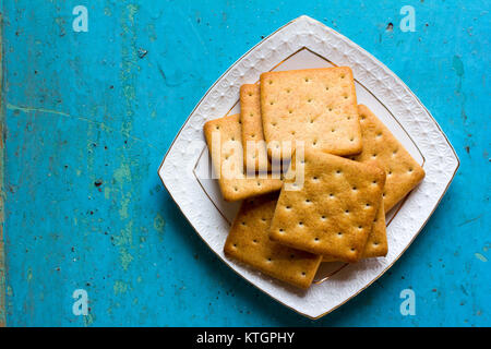 Cracker Kekse in eine weiße Keramik square Untertasse auf alten blauen Hintergrund. Freier Platz für Text. Platz kopieren. Top View Stockfoto