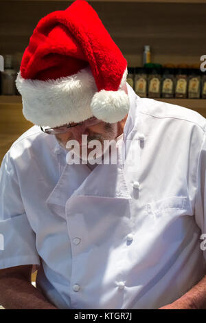 Älterer Mann mit Bart in Chef weiß und ein Santa hat die Zubereitung von Speisen in einer Küche in der Weihnachtszeit Stockfoto