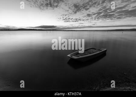 Ein kleines Boot in der Mitte des perfekt noch Wasser bei Sonnenuntergang, mit Makrelen wolken himmel (See Trasimeno, Umbrien, Italien) Stockfoto