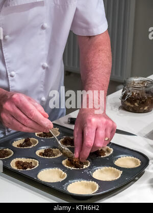 Ältere Mann in Chef weiß Füllung Mince Pie Fällen bereit zum Backen zur Weihnachtszeit in einer Küche Stockfoto