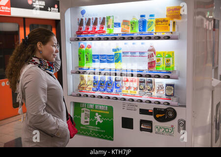 JAPAN, KYOTO - CA. APR, 2013: Europäische Frau steht in der Nähe von japanischen Automaten mit Softdrinks und wählt die Getränke. Traditionelle Getränkeautomat, Safe Stockfoto