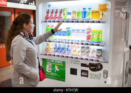 JAPAN, KYOTO - CA. APR, 2013: Europäische Frau steht in der Nähe von japanischen Automaten mit Softdrinks und versucht, Getränke zu kaufen. Traditionelle Getränkeautomat, Safe Stockfoto