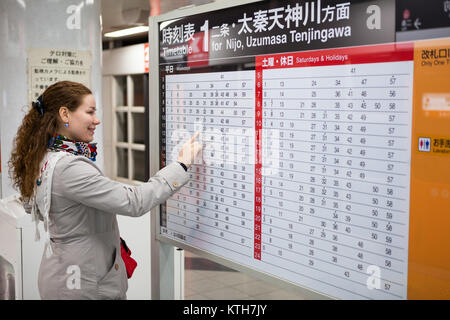 JAPAN, KYOTO - CA. APR, 2013: Europäische Frau sieht der japanischen U-Bahn Fahrplan. Informationen Schreibtisch mit Tarifen. Kyoto städtische U-Bahn ist die Metro Stockfoto