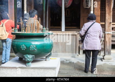 JAPAN, KYOTO - CA. APR, 2013: Asiatische Besucher beten im Bereich der Kinkaku-ji-Schrein. Vase für brennende Kerzen ist auf dem Gebiet der Rokuon-ji oder Golden Pavili Stockfoto