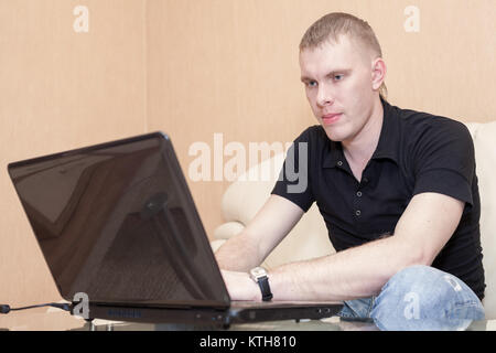 Stattlichen Kaukasischen blonder Mann beobachten Bildschirm mit einem Lächeln auf dem Gesicht, mit Laptop zu Hause Stockfoto