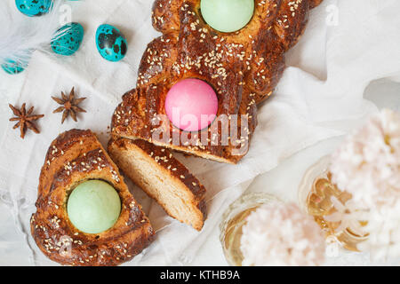 Traditionelle griechische Ostern Brot - tsoureki, in Ostern Dekoration mit bemalten Eiern und Blumen in Scheiben geschnitten. Ostern Festival Konzept. Stockfoto