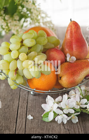 Frucht, Birne, Grapefruit, Zitrone, Pfirsich, erdbeere in einem Korb auf dem Hintergrund einer Blumenstrauß aus kleinen weißen Blüten an einem sonnigen Tag. Die vertikale Rahmen Stockfoto