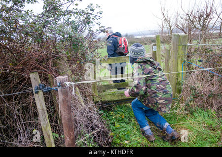 Zwei Wanderer versuchen, hinter einem elektrischen Zaun vor einem öffentlichen Fußweg und Stil in Felder in der Landschaft im Winter zu erhalten Stockfoto