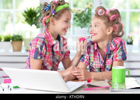 Zwei niedliche kleine Mädchen mit Laptop am Tisch sitzen und sich verschönern Stockfoto