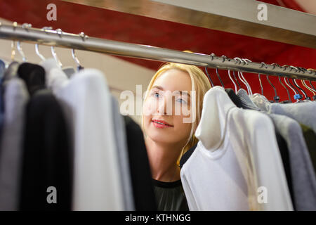 Junge Frau wählt Kleidung im Store. Closeup Portrait von Kunden in der Nähe von Wäscheständer in der Mode Boutique. Shopping Konzept Stockfoto