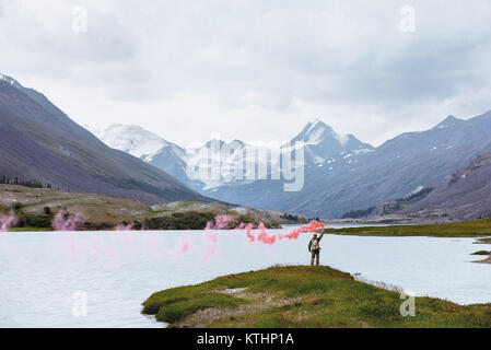 Man steht mit roten Signal Feuer auf dem Hintergrund der schönen Berg See und Gletscher Stockfoto