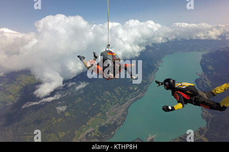 Dieses Tandem skydiving Paar, plus den Spaß Jumper sind, genießen Sie die tolle Aussicht über den schönen See und Berg. Die smiley-Gesichter prüfen! Stockfoto