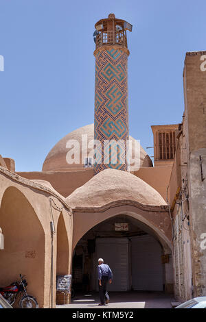 Yazd, Iran - 22. April 2017: Ein älterer Mann geht unter der gewölbten Eingang eines Ton Gebäude mit einem Minarett. Stockfoto