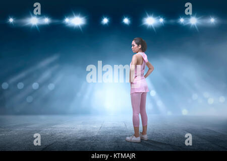 Jungen asiatischen runner Frau stehend auf Betonboden mit Spot hellen Hintergrund Stockfoto