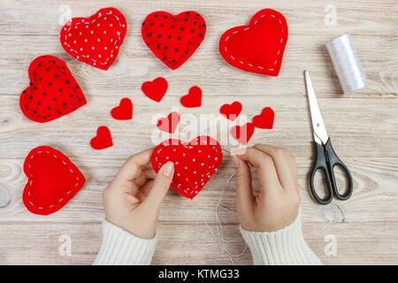 Valentinstag Thema. Arbeitsplatz für die Vorbereitung handgefertigte Dekorationen. Blick von oben auf die weiblichen Händen fühlte Herzen nähen. Verpackte Geschenke, Werkzeuge schäbigen Holztisch. Stockfoto