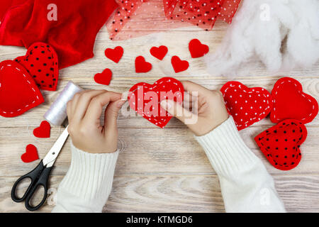 Valentinstag Thema. Arbeitsplatz für die Vorbereitung handgefertigte Dekorationen. Blick von oben auf die weiblichen Händen fühlte Herzen nähen. Verpackte Geschenke, Werkzeuge schäbigen Holztisch. Stockfoto