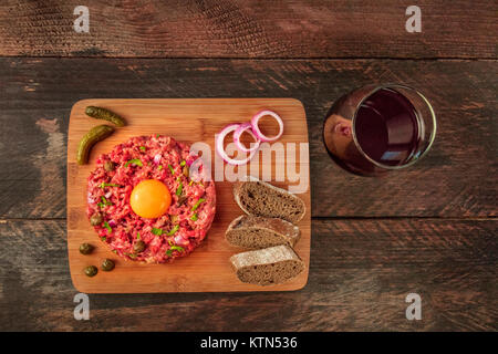 Ein Foto von einem Steak Tartar mit einem rohen Eigelb, Roggenbrot, und lila Zwiebeln, geschossen von oben auf einen dunklen rustikalen Textur mit einem Platz für Text Stockfoto