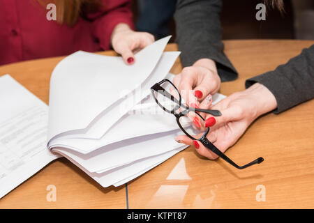 Schließen Sie herauf Bild von einem Schreibtisch mit Brille und auf der it und Arme von zwei Business Frauen lesen Sie Stockfoto