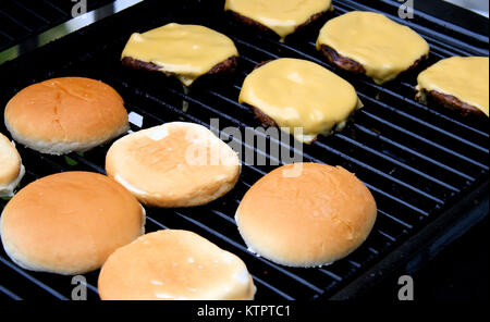 Hamburger Pastetchen mit verarbeitetem Käse kochen auf einem Tisch im Freien top Grill. Brötchen Schiebeschalter neben Stockfoto