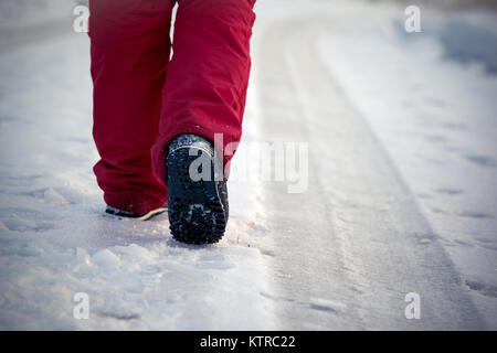 Wandern im eisigen Winter auf der vereisten Straße durch Anschluss von Autos in roten Hosen und Schnee Stiefel Stockfoto