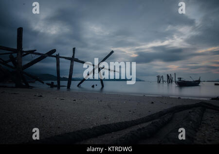 Bewölkt Tag am Alten und Schäden Bootsanleger am schwarzen Sandstrand in Langkawi Malaysia. Aufgrund von Erosion und Big Wave, der Steg hatten Schäden und nie repariert. Stockfoto