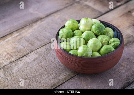 Raw Rosenkohl in Keramik Schüssel auf rustikalen Holztisch. Stockfoto