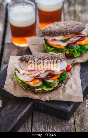 Roggen Sandwiches mit Schinken und letucce auf Holz Tisch mit zwei Gläsern Bier Stockfoto