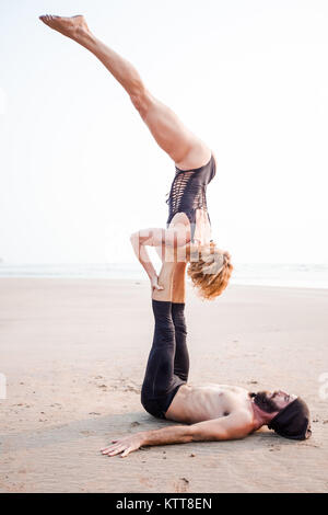 Paar schöne Menschen üben acro Yoga am Strand bei Sonnenuntergang in Goa, Indien Stockfoto