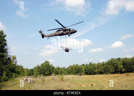 Soldaten der Batterie B, 1st Battalion, 258Th Field Artillery für Ihre 105-mm-Haubitze durch eine New York National Guard UH-60 Blackhawk Hubschrauber aus Army Aviation Support Fazilität 3 in Latham, New York, zu einem vorher festgelegten Gebiet am Fort Drum, NEW YORK, während einer "trockenen" feuerwehrübung zu geflogen werden, warten Stockfoto