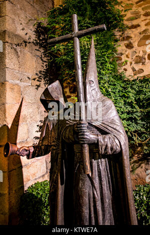Statue von einem Mönch mit einer Glocke und einem spitzen Haube (capirote) Mönch, ein Kruzifix in Caceres, Extremadura, Spanien Stockfoto