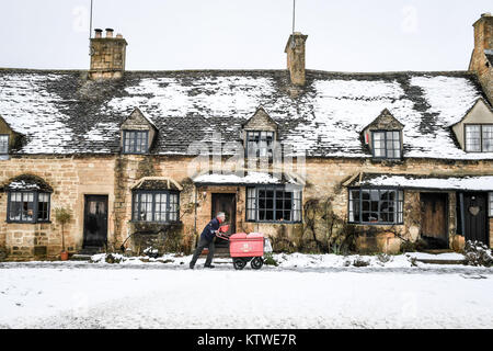 Ein Postbote schiebt seinen Wagen vorbei an verschneiten Häuschen auf der High Street in Broadway, Worcestershire, nachdem über Nacht Schnee hat Travel Störungen über Teile der britischen verursacht. Stockfoto