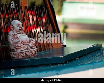 Nahaufnahme der dekorative Keramik Buddha/Budai sitzen auf dem Dach eines schmalen Boot auf dem Fluss (Outdoor) mit unscharfen Hintergrund Stockfoto