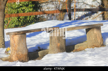 Eine Bank, die mit Baumstämmen im Schnee Stockfoto