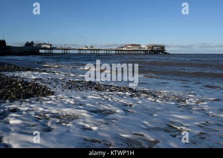 Cromer, Norfolk, Großbritannien. Wellen auf den Strand bei Cromer mit Cromer Pier im Hintergrund, ist das Zuhause der RNLI Cromer Rettungsboot Station Stockfoto