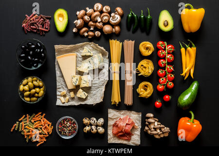 Verschiedene frische Zutaten zum Kochen italienische Pasta, Spaghetti, Fettuccine, Fusilli und Gemüse auf einem schwarzen Hintergrund. Flach, Ansicht von oben. Stockfoto