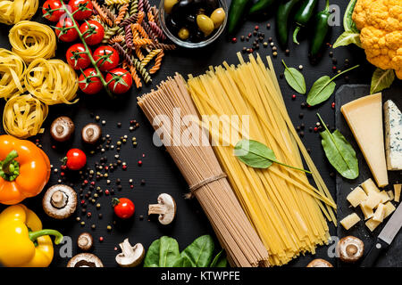 Verschiedene frische Zutaten zum Kochen italienische Pasta, Spaghetti, Fettuccine, Fusilli und Gemüse auf einem schwarzen Hintergrund. Flach, Ansicht von oben. Stockfoto