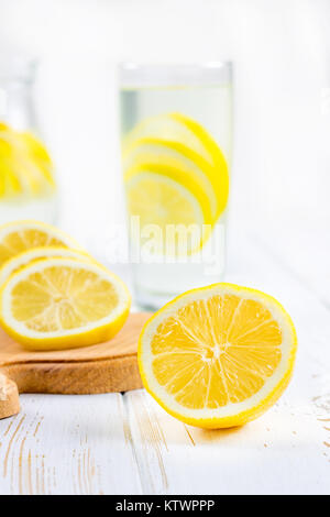 Ein Becherglas und einen Krug kalten Limonade auf einem weißen Hintergrund Holz umgeben von Zitronen Stockfoto