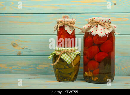 Nahaufnahme von drei Gläsern der rustikalen hausgemachte Pickles, Gurke Gurken, Tomaten und Paprika Salat, mit Bettwäsche textile Deckel Dekorationen und Jute Stockfoto