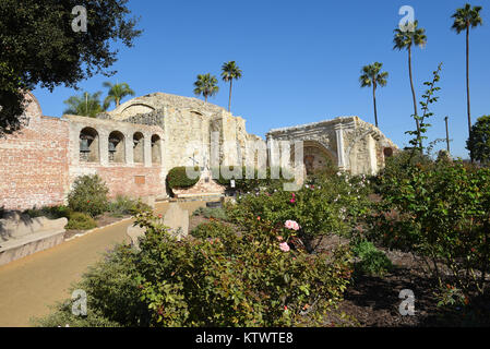 San Juan Capistrano, Ca - Dezember 1, 2017: Mission Bell Wand- und Serra Statue mit den Ruinen der großen Stein Kirche mit Rosengarten im foregr Stockfoto