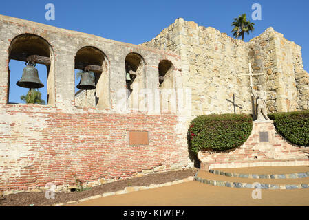 San Juan Capistrano, Ca - Dezember 1, 2017: Mission Bell Wand- und Serra Statue mit den Ruinen der großen Stein Kirche. Stockfoto