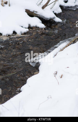 Kleiner Bach fließt durch den Schnee mit kleinen Felsvorsprung von Vereisung. Stockfoto