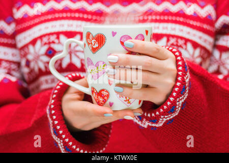 Frau in rot pullover hält einen Winter Cup mit Herzen. Winter und Weihnachten Konzept. Stockfoto