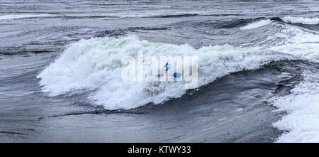 Eine behelmte Mann in einem Kajak verschwindet fast in eine riesige Welle an Sechelt Rapids, eines der schnellsten Gezeiten der Welt vergeht (British Columbia). Stockfoto