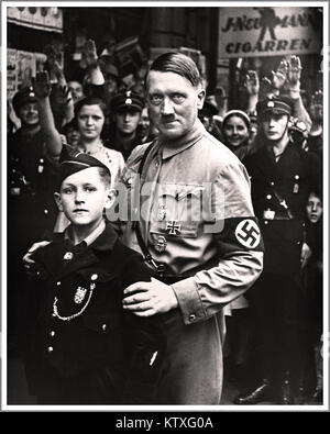 HITLER-Nazi-Deutschland-Propagandabild Adolf Hitler des 1930er NS-Diktators Adolf Hitler trug NSDAP-Uniform und Hakenkreuzarmband in Berlin und posierte mit einem erschreckenden Ausdruck neben einem 10-12-jährigen jungen Mitglied der Hitler-Jugend-Organisation Hitler-Jugend. Die Menge hat Heil Hitler gegrüßt. Stockfoto